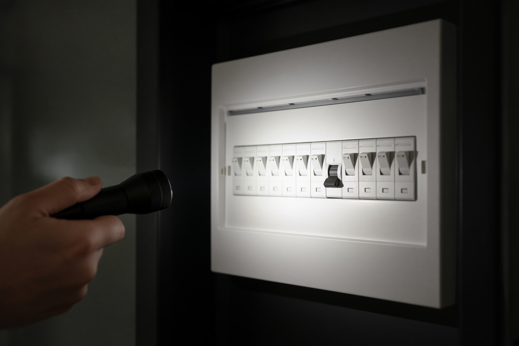 Hand checking the trip switches on a UK consumer unit with a torch